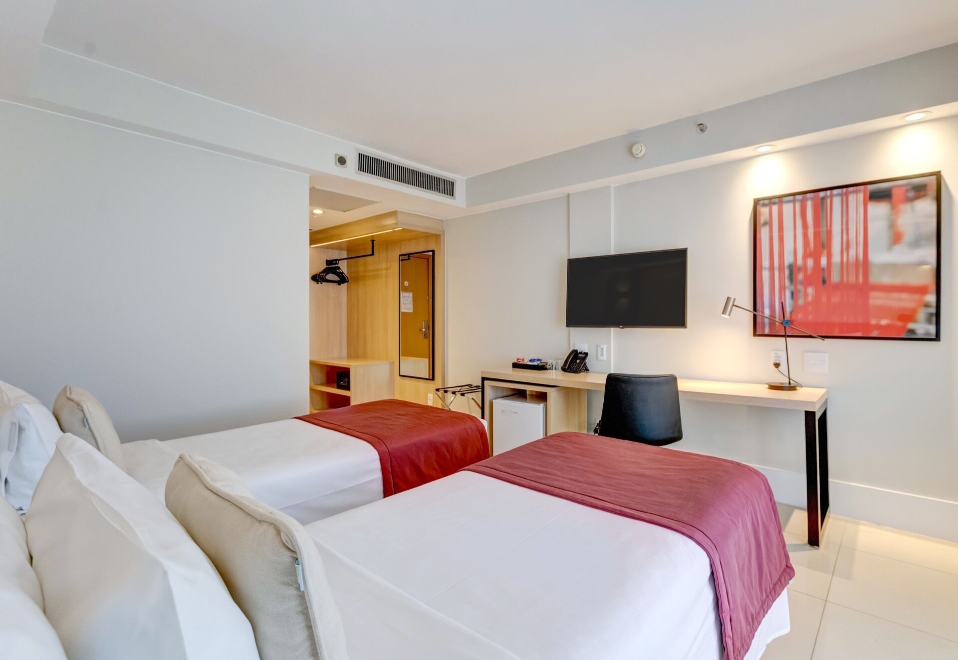 Habitación de hotel con dos camas, un escritorio, una silla, un televisor y un cuadro en la pared.