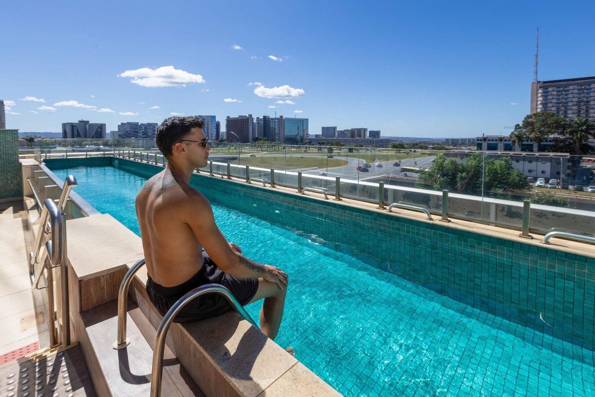 A man sitting by a swimming pool with a cityscape in the background.