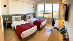 Hotellihuone, jossa on kaksi sänkyä, työpöytä, tuoli, televisio ja ikkuna, josta on näkymä kaupunkiin.