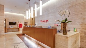 Vastaanottotiski, jossa on puinen tiski, ruukkuorkidea ja kyltti, jossa lukee ”RAMADA”.
