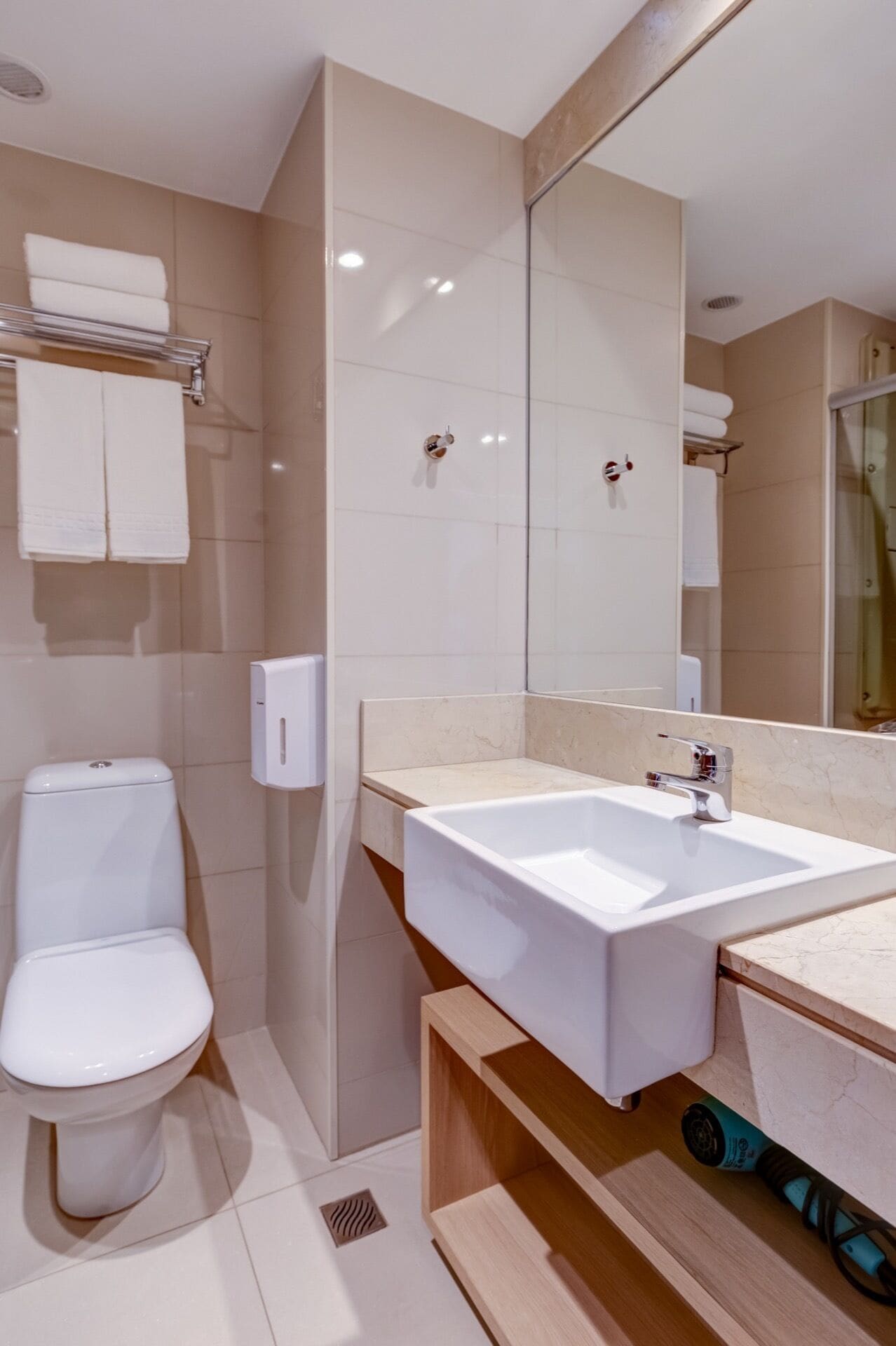 A modern bathroom with a white toilet, a large mirror, and a white sink.
