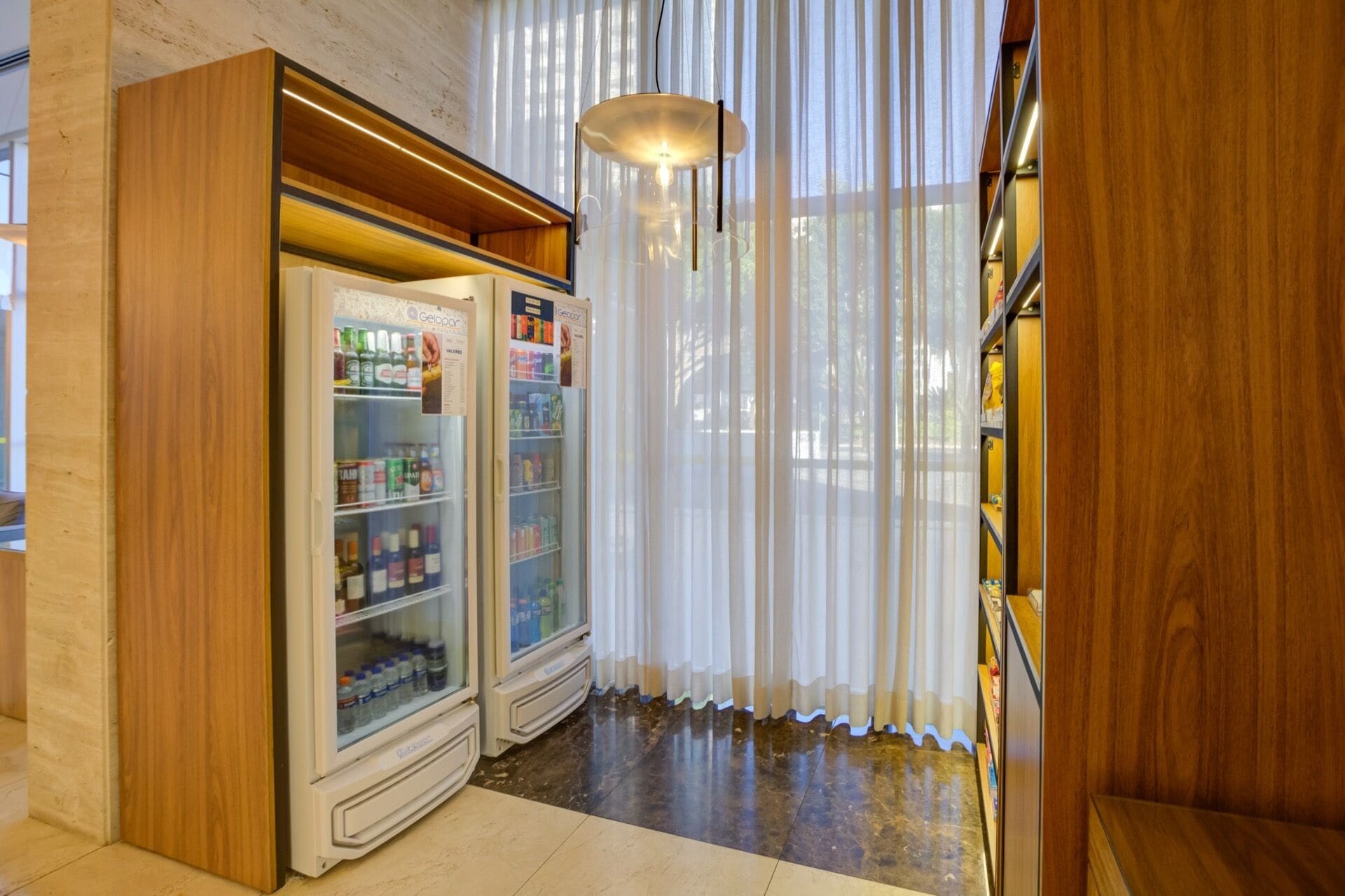 Ein Zimmer mit zwei Getränkespendern, einem Holzschrank und einem großen Fenster mit durchsichtigen Vorhängen.