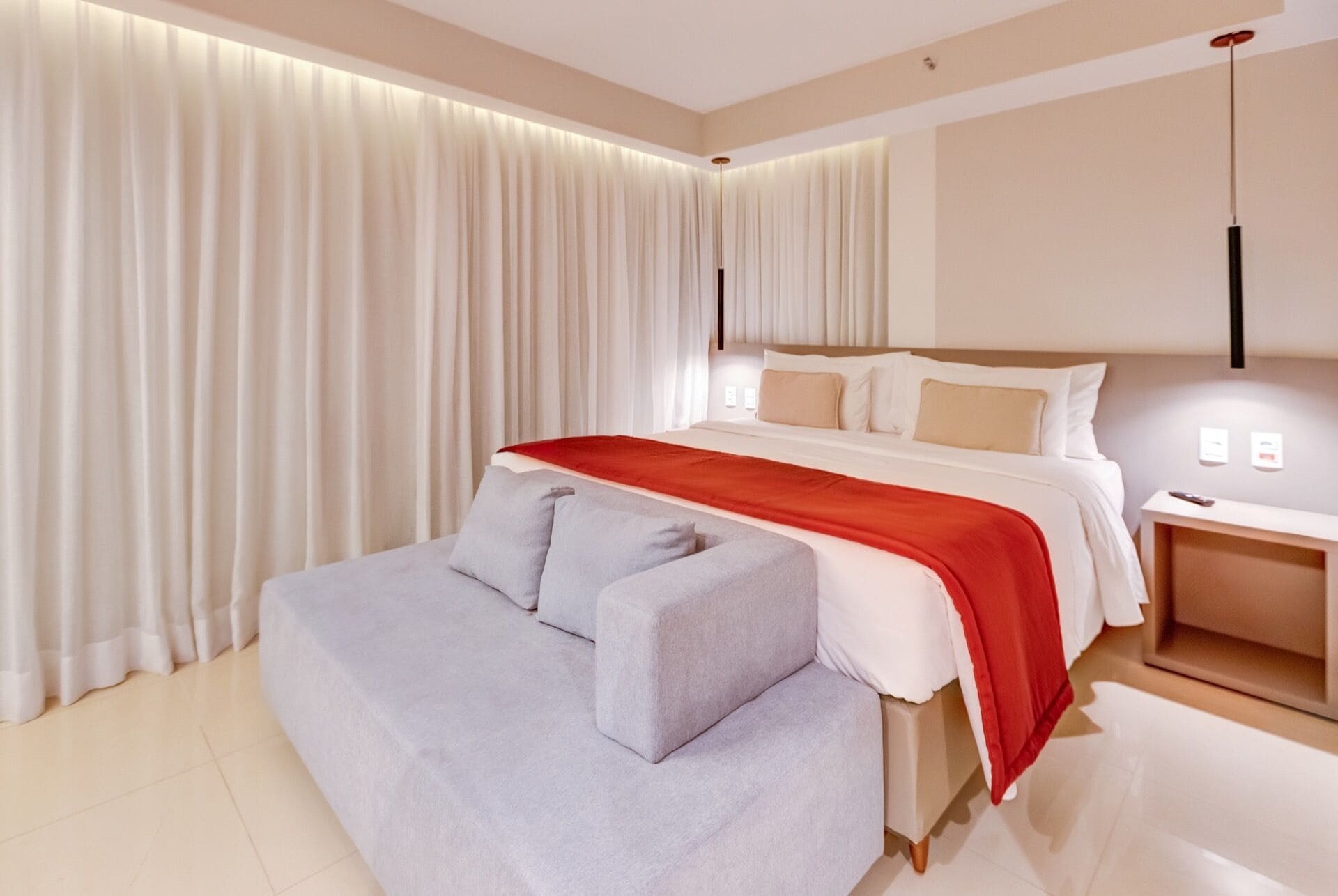 Une chambre d’hôtel moderne avec un grand lit, un canapé gris et une table de chevet avec une lampe.