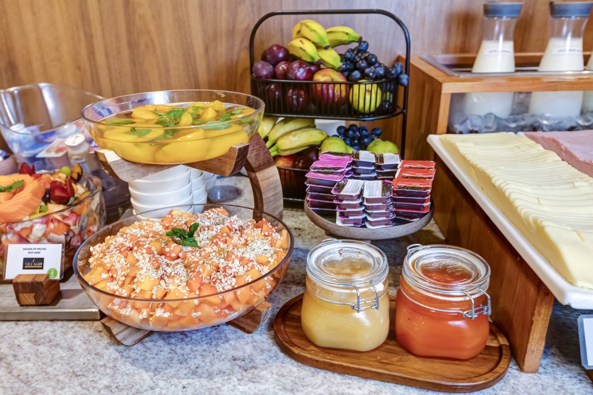 Un bufé con distintos alimentos, incluyendo frutas, una ensalada de frutas y postres.