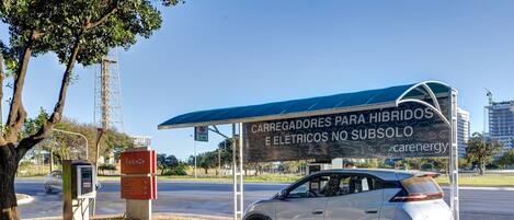 A car charging station with a sign for hybrid and electric vehicles, a car parked nearby, and a covered area with a blue roof.