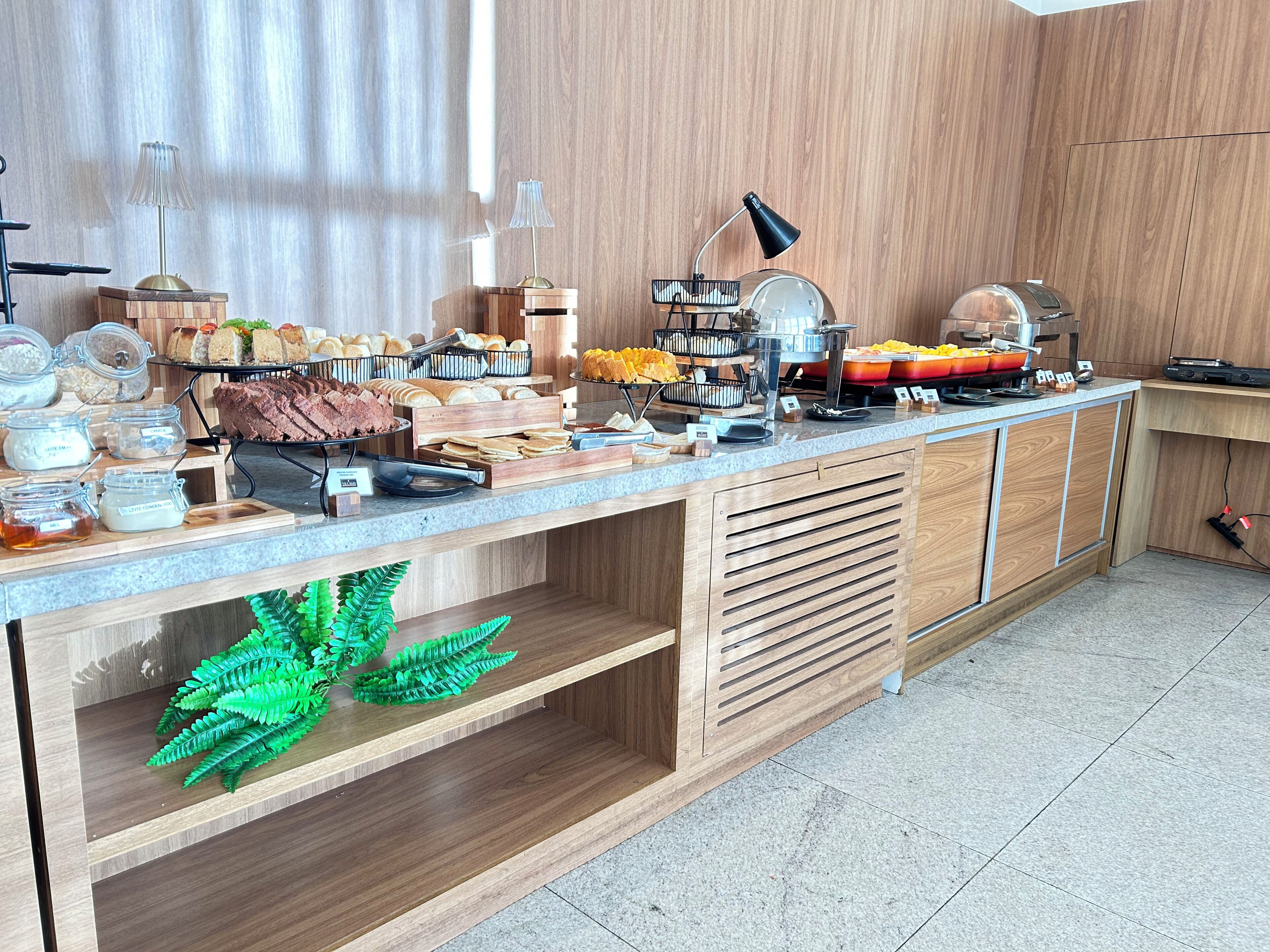 A buffet setup with various food items and condiments, a coffee machine, and a decorative plant.