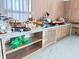 Montaje tipo bufé con diversos alimentos y condimentos, una máquina de café y una planta decorativa.