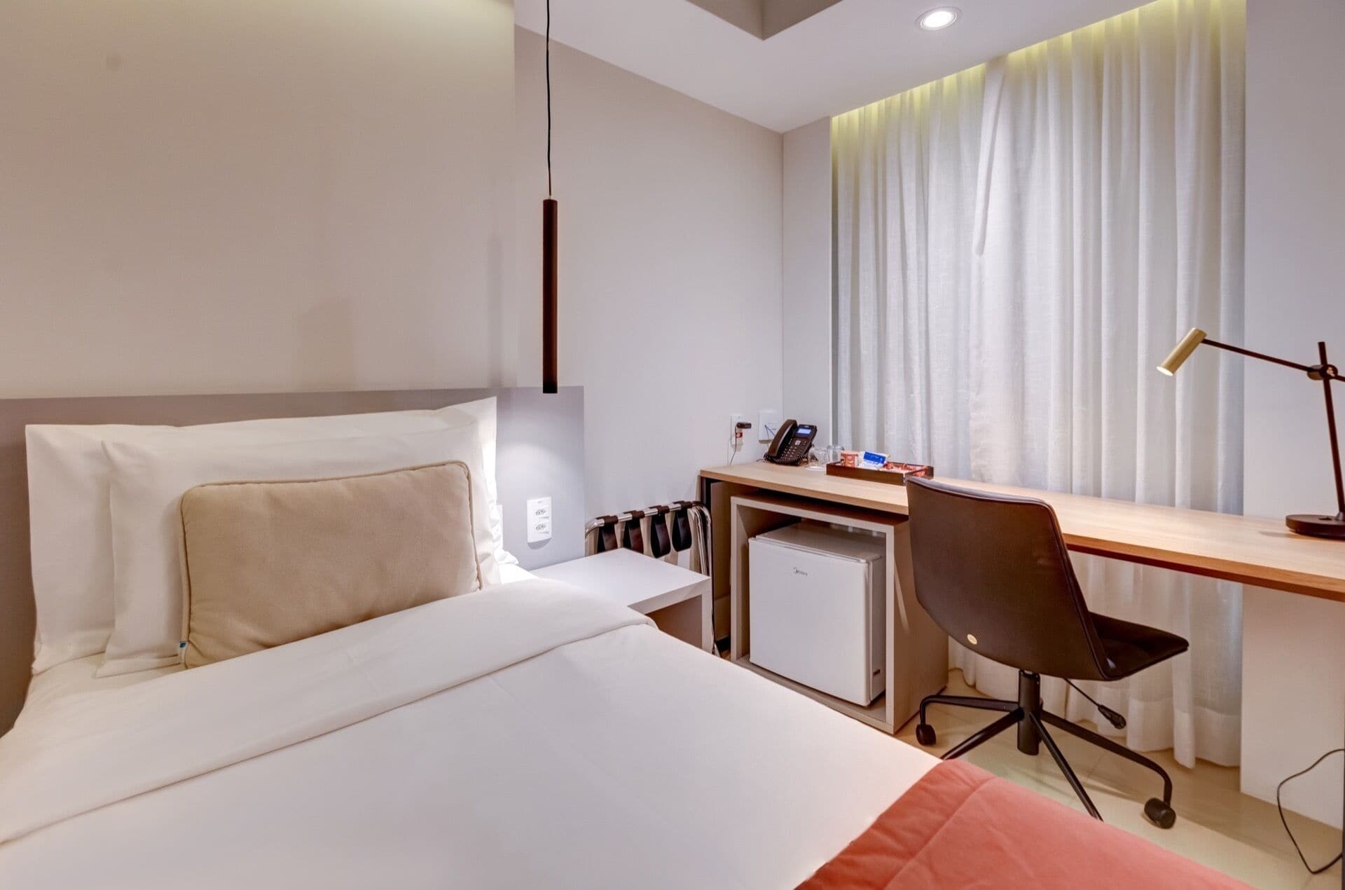 Ein Hotelzimmer mit Bett, Schreibtisch, Stuhl und einem kleinen Kühlschrank.