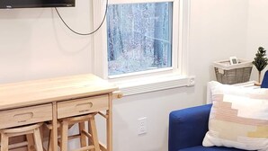 Ein Zimmer mit einem Holztisch, einem blauen Sofa, einem an der Wand montierten Fernseher und einem Fenster mit einem 'hello' Schild darüber.