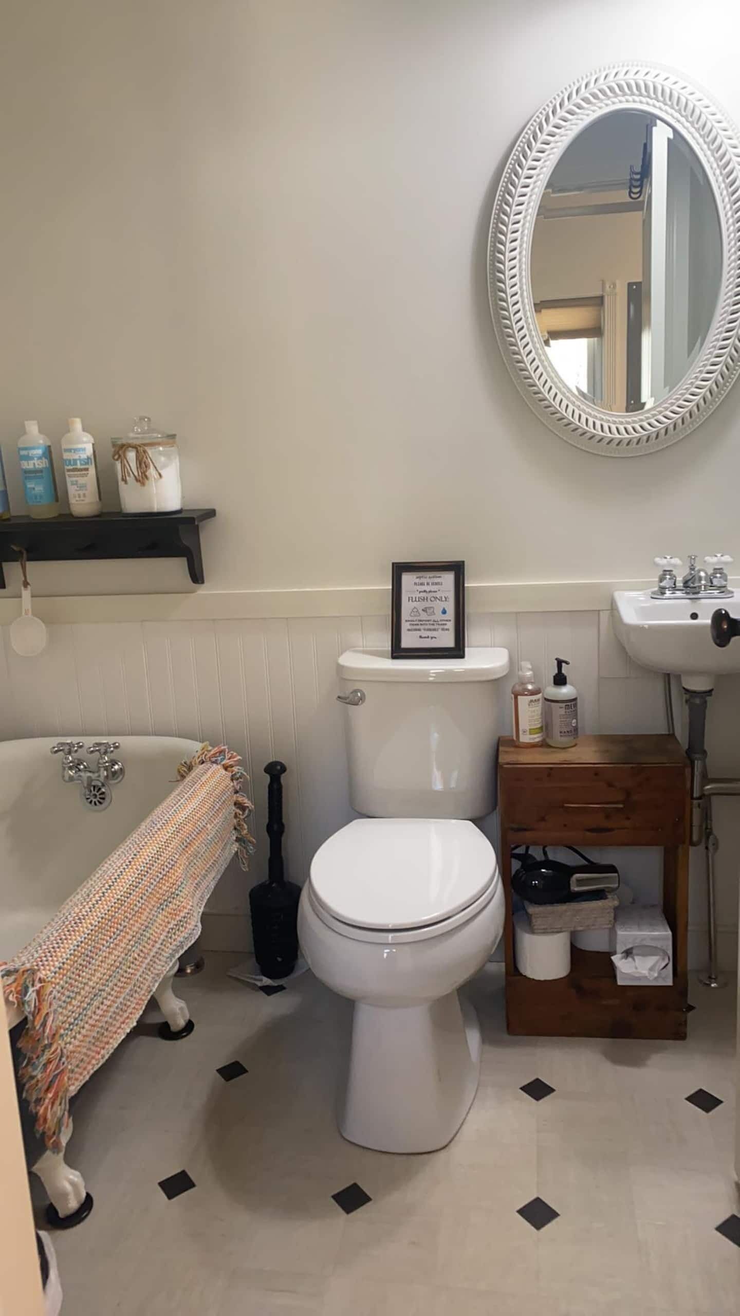 Un bagno con servizi igienici, lavabo e vasca da bagno. C'è uno scaffale con articoli da toilette e un cartello incorniciato sopra il water.