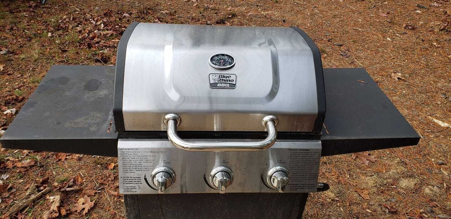 Ein Grill aus Edelstahl mit Tragegriff und drei Reglern, aufgestellt auf einer ebenen Fläche im Freien.