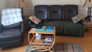 Una sala de estar con un sofá de cuero negro, una pequeña mesa de centro de madera, un sillón negro y una manta estampada.