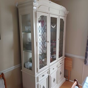 A white, ornate cabinet with multiple glass-fronted drawers and doors, containing various kitchen items.