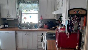Una cocina con armarios blancos, un refrigerador rojo y una ventana con cortina estampada.