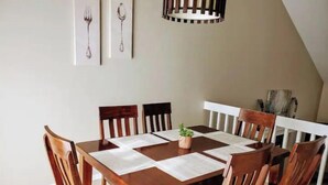 A dining area with a wooden table and chairs, a small plant on the table, and framed pictures on the wall. - West Omaha Gem • Near Trails, Parks & Dining ❤ (Omaha)