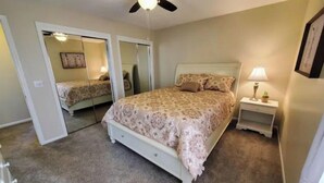 A bedroom with a bed, a nightstand, a ceiling fan, and a mirror. - West Omaha Gem • Near Trails, Parks & Dining ❤ (Omaha)