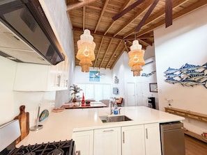 Una cocina con isla central, armarios blancos, un lavamanos de acero inoxidable y una estufa a gas.