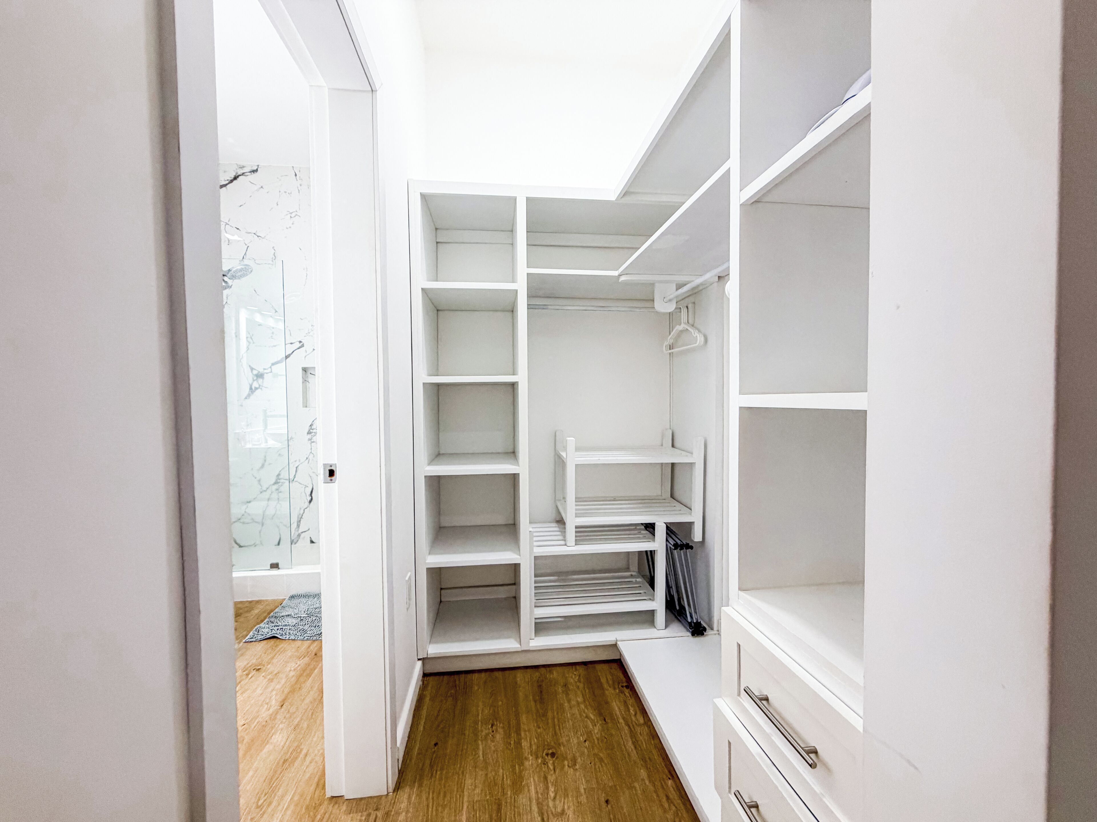 A walk-in closet with open shelves, a hanging rod, and a bench.