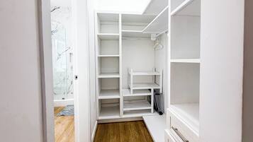 A walk-in closet with open shelves, a hanging rod, and a bench.