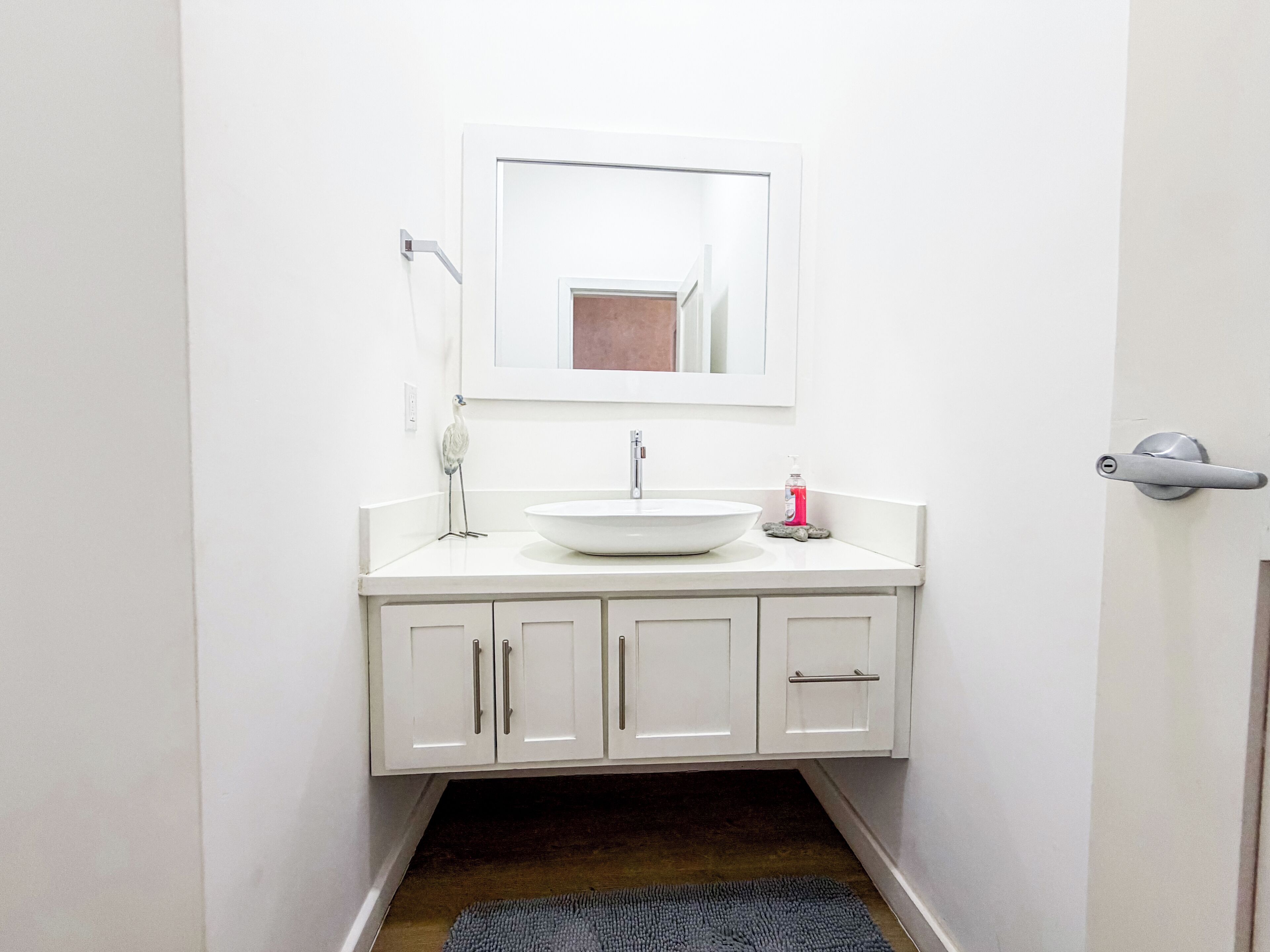 Une petite salle de bain avec un lavabo blanc, un miroir et des placards.