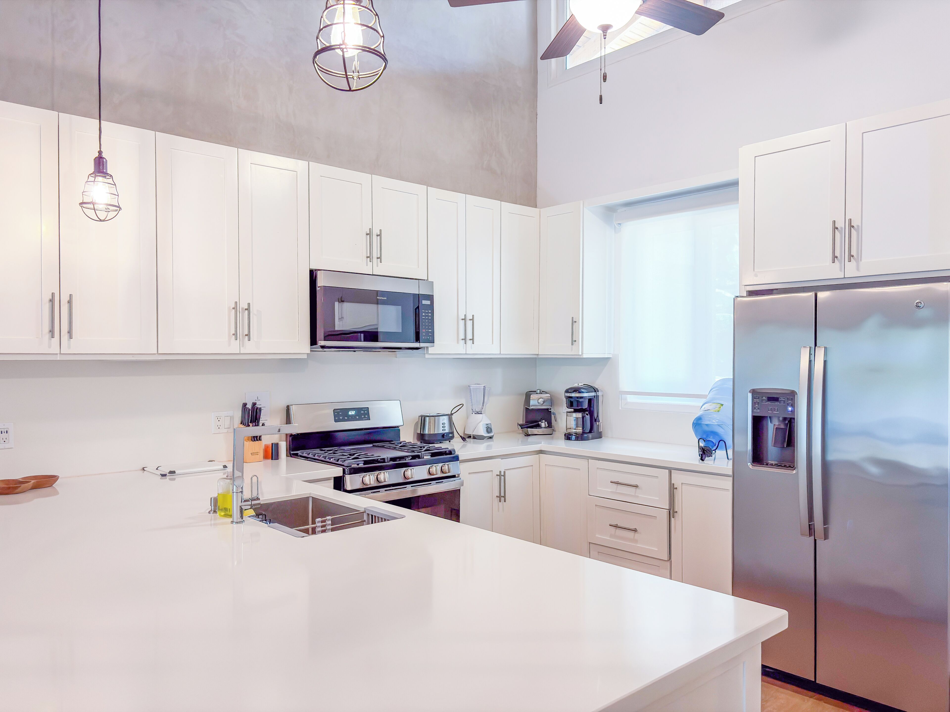 Una cocina moderna con armarios blancos, electrodomésticos de acero inoxidable e iluminación colgante.