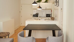 A modern kitchen with a central island, pendant lighting, and a dining area with a dark table and upholstered chairs.