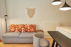 A modern living room with a grey sofa, patterned cushions, a round armchair, a wooden side table, and pendant lighting.