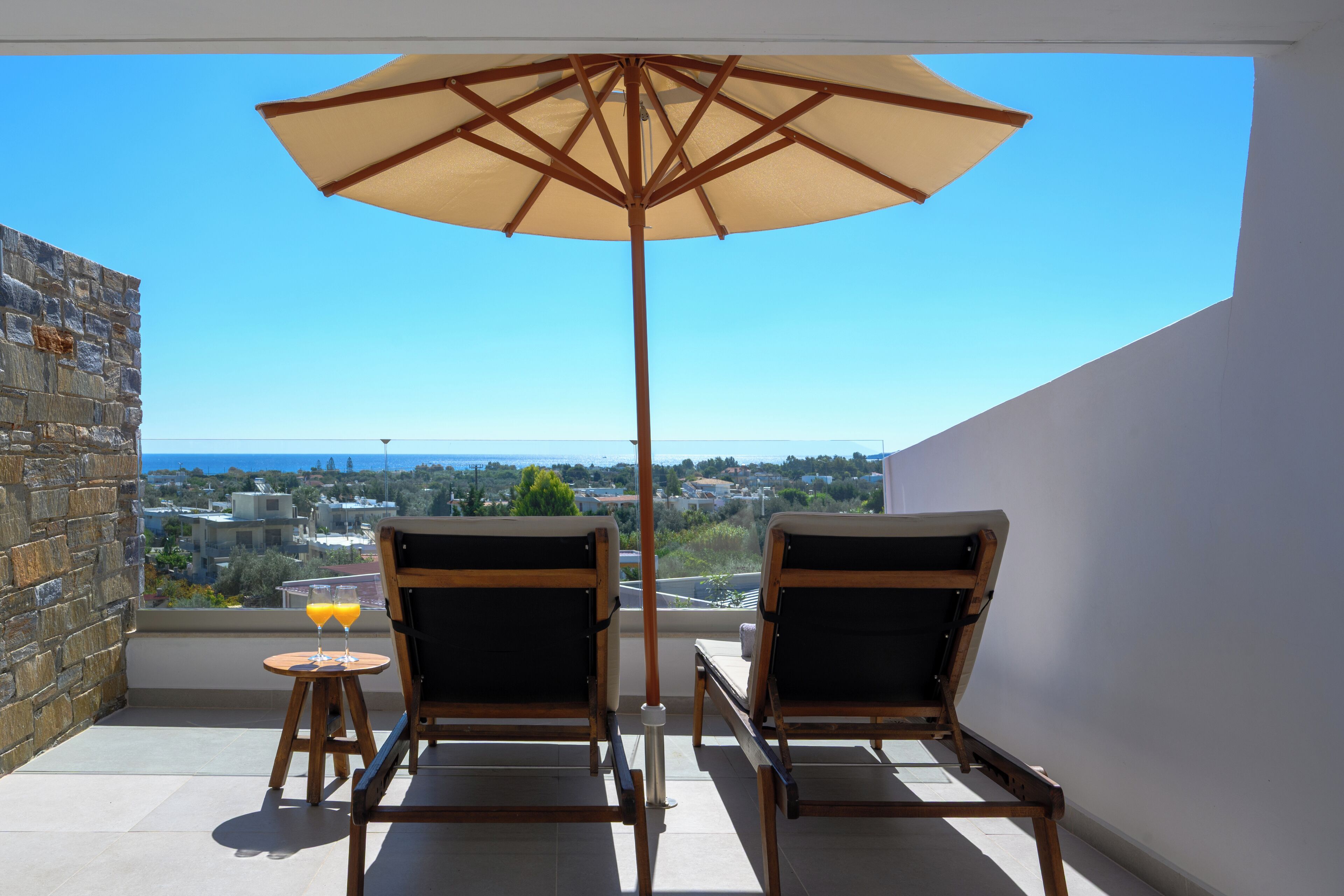 Un balcon avec deux chaises en bois et un grand parasol, donnant sur un paysage urbain.