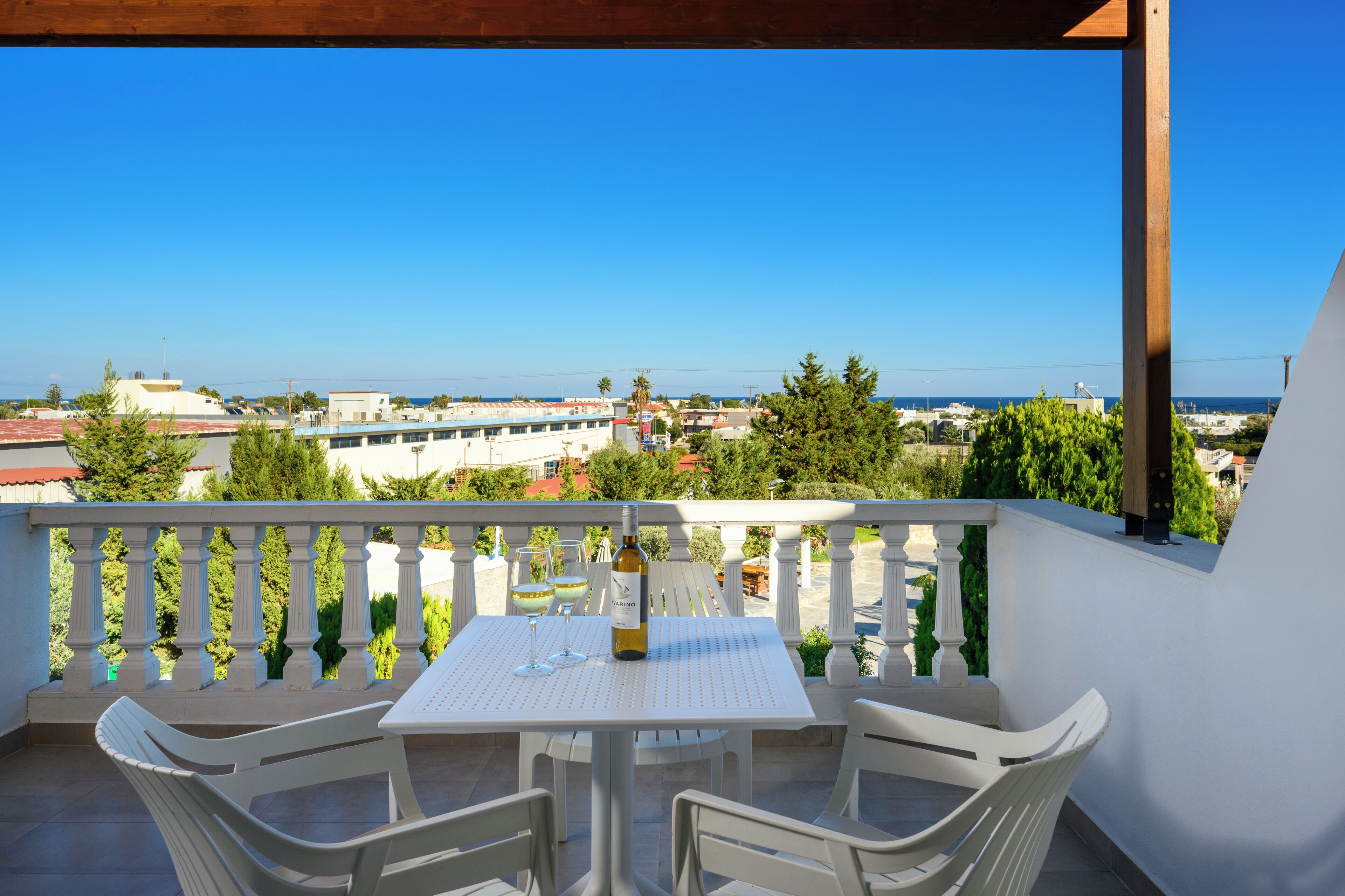 A balcony with a white table and chairs, overlooking a cityscape and the sea.