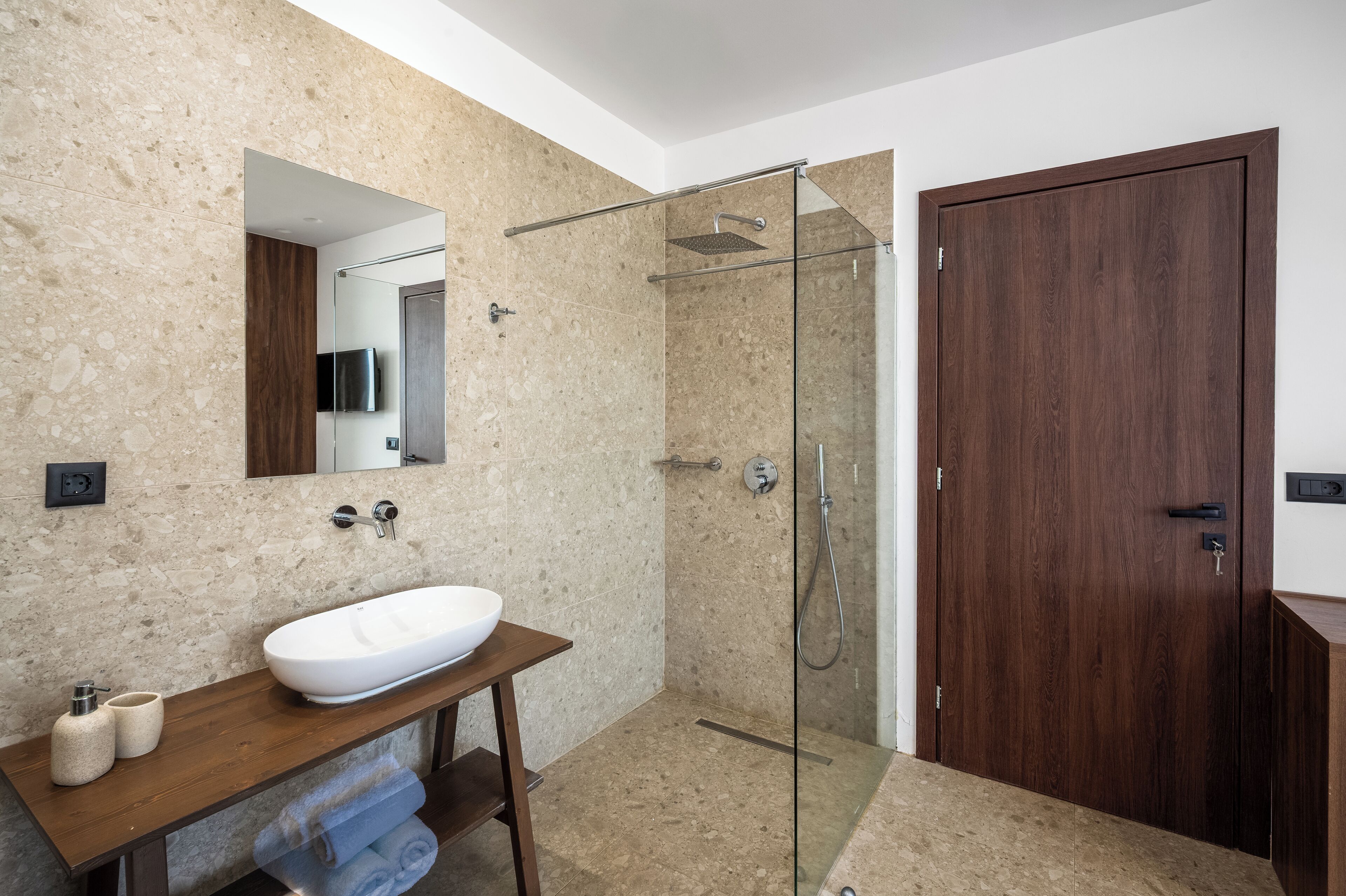 Ein modernes Badezimmer mit einem freistehenden Waschbecken, einer Glaskabine zur Dusche und einer Holztür.