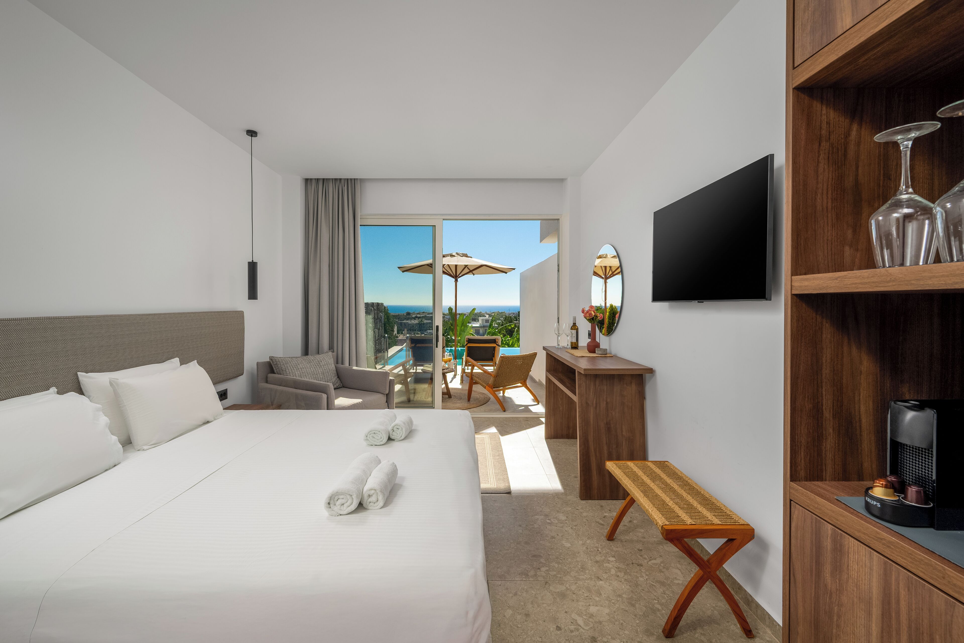 A hotel room with a large bed, a desk, a TV, and a balcony with a view.