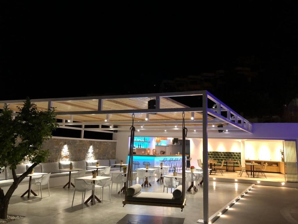 An outdoor seating area with tables and chairs, a swing, and a bar area in the background.