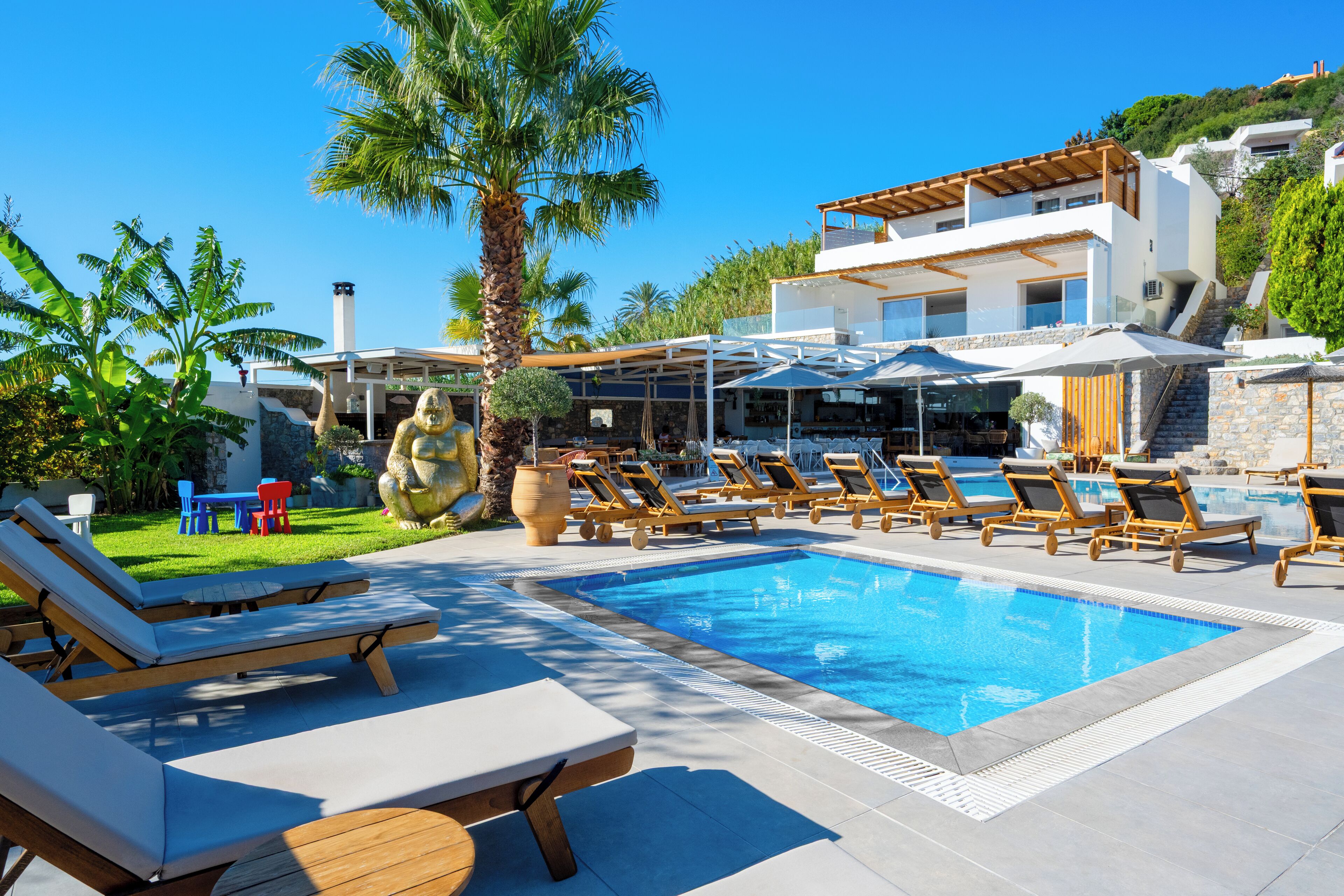 A poolside area with lounge chairs, umbrellas, and a modern house in the background.