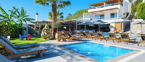 A poolside area with lounge chairs, umbrellas, and a modern house in the background.