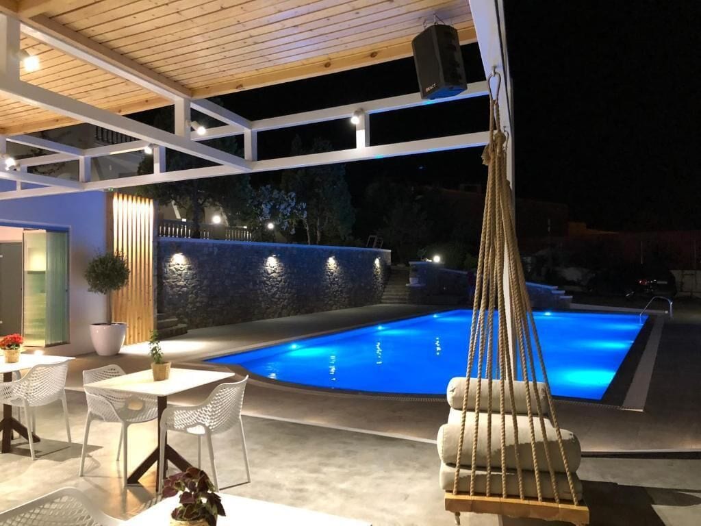Een buitenzwembad met een hangstoel, tafels en stoelen.