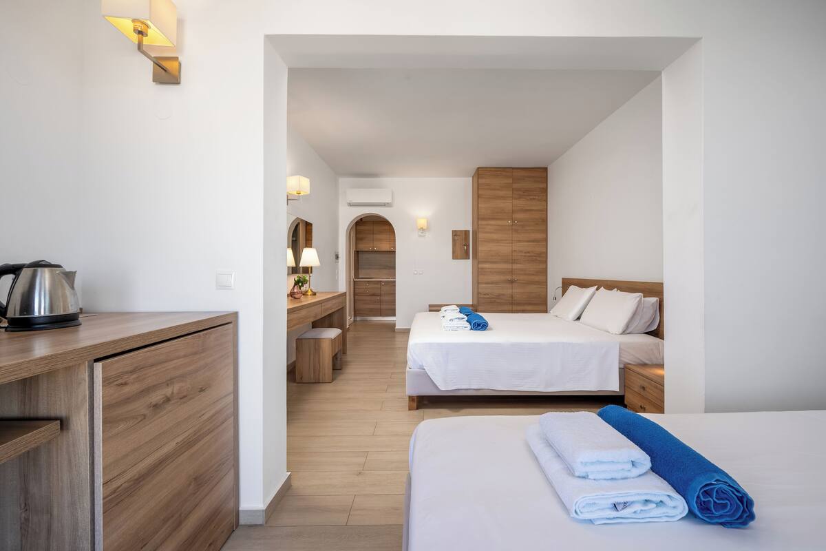 Une chambre d’hôtel avec deux lits, un bureau en bois, une kitchenette et une salle de bain avec douche.