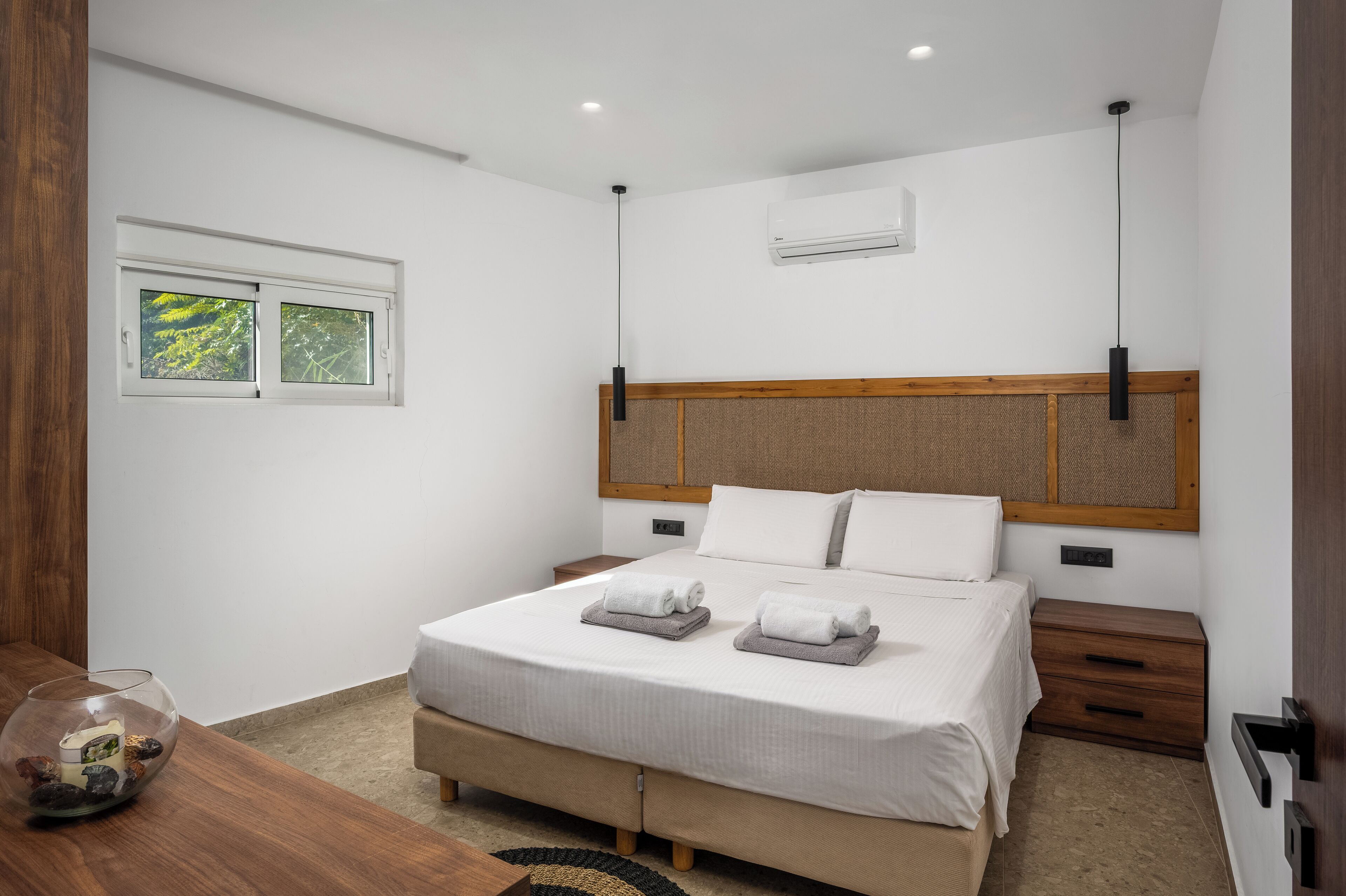 Un dormitorio moderno con una cama grande, cabecera de madera, mesitas de noche y una ventana con vistas a la vegetación.