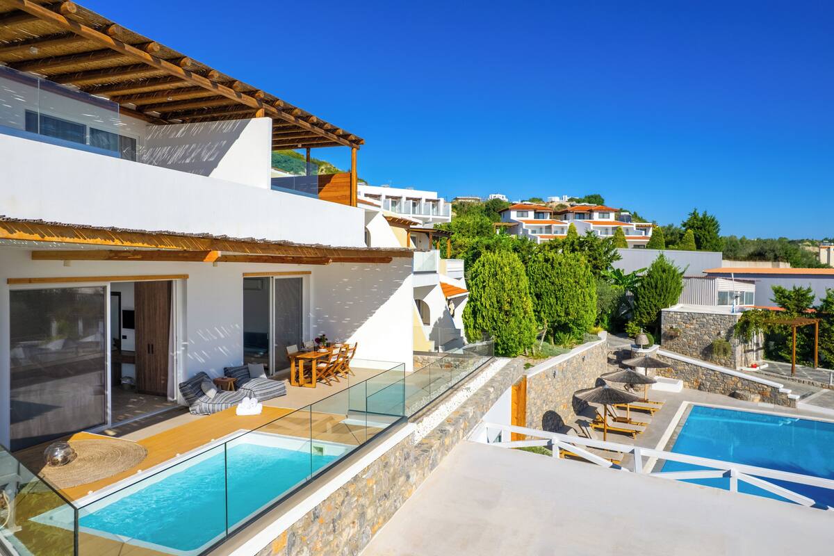 Une villa moderne dotée d’une piscine intérieure à panneaux de verre, d’un espace extérieur aménagé et offrant une vue sur les bâtiments voisins.