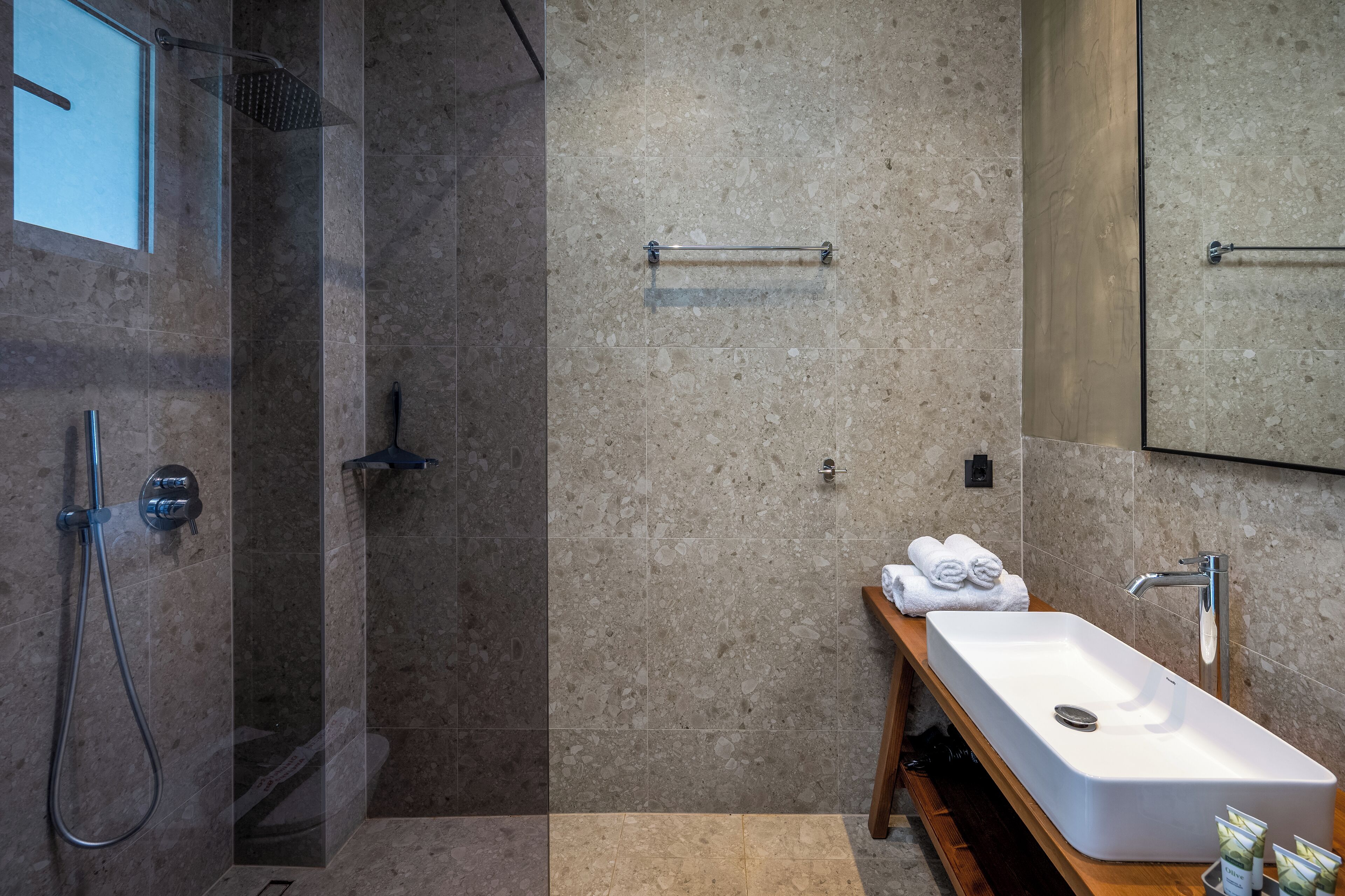A modern bathroom with a glass-enclosed shower, a wooden vanity with a sink, and a towel rack.