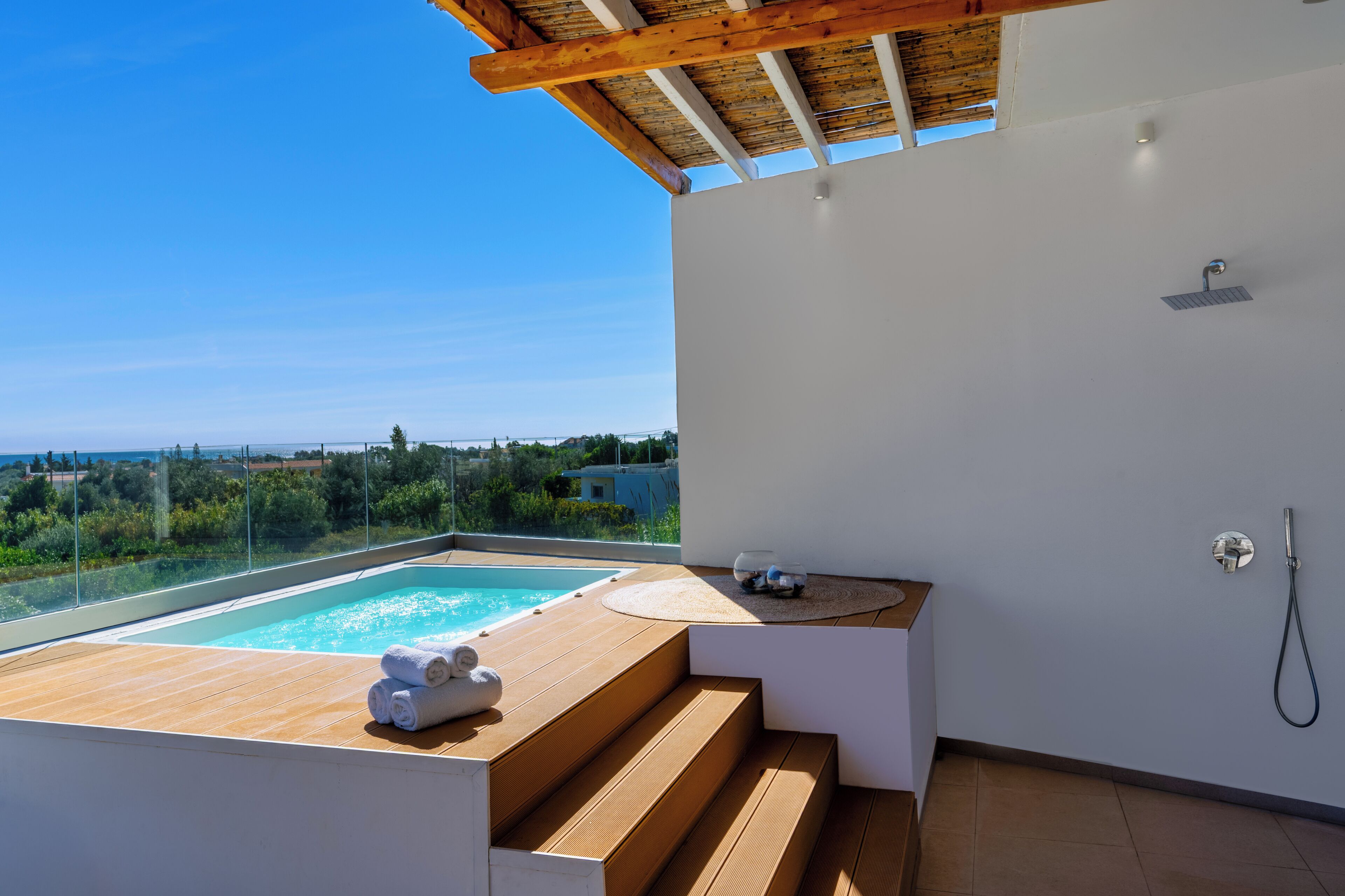 A modern bathroom with a wooden deck, a built-in hot tub, and a view of the sea.