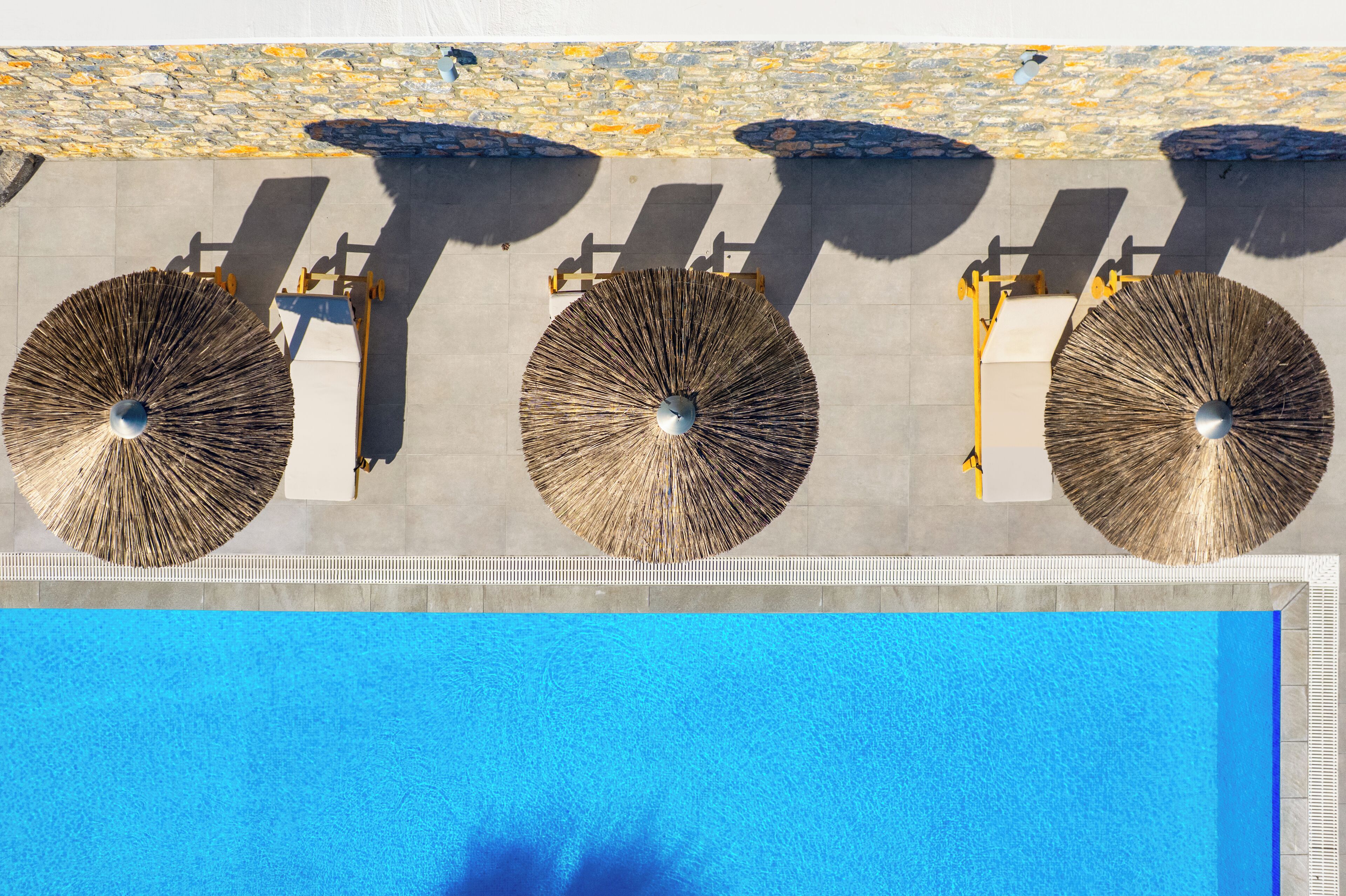 Ein Schwimmbecken mit drei Sonnenschirmen und Liegestühlen.