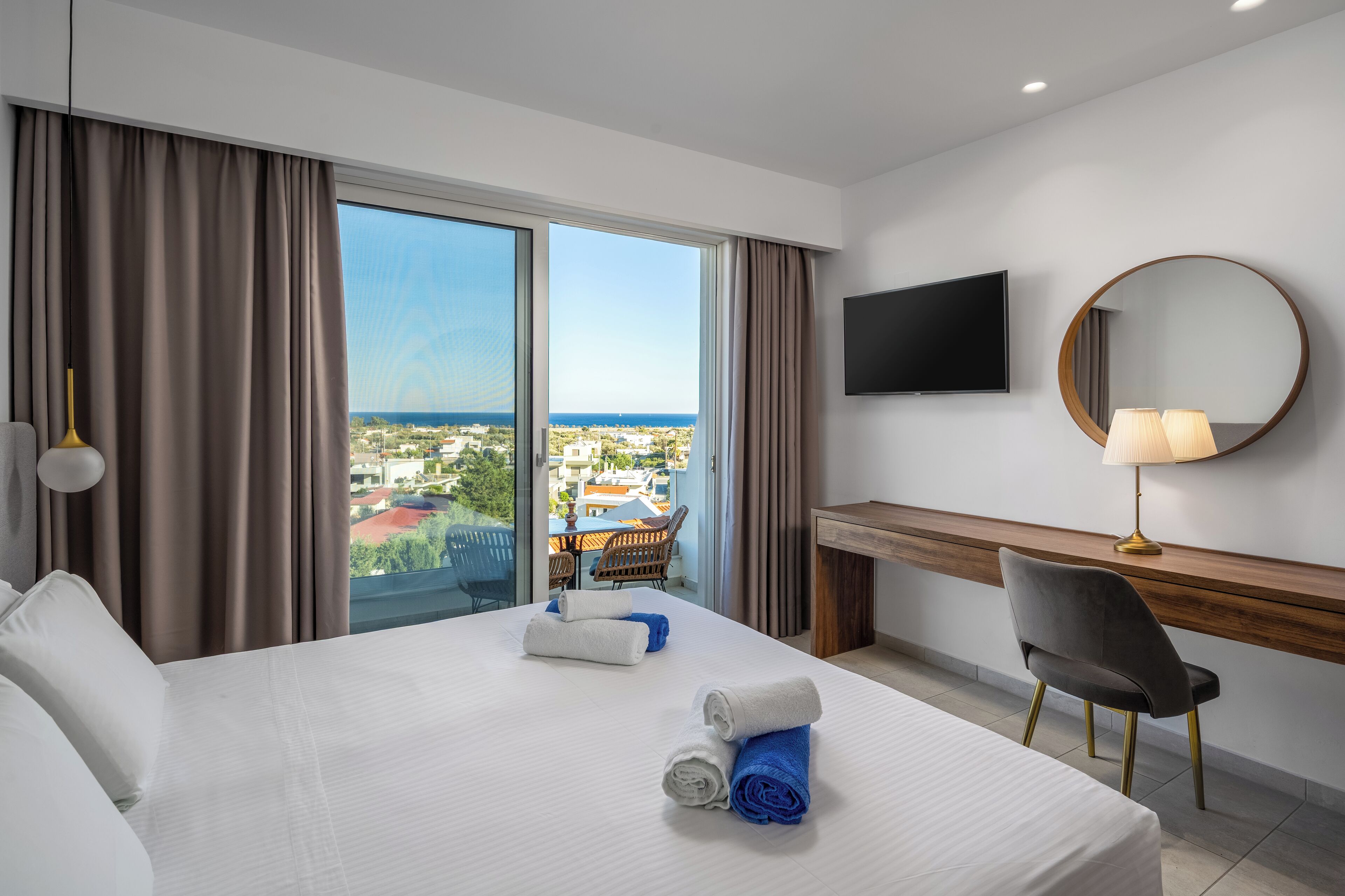 A hotel room with a large bed, a desk, a chair, a TV, and a view of the city through the window.