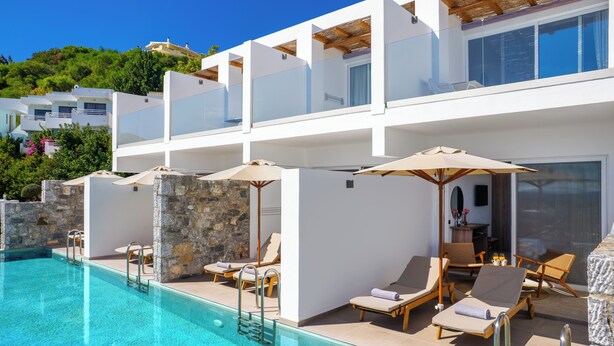 Un hôtel moderne doté d’une piscine, de chaises longues et offrant une vue sur une colline.
