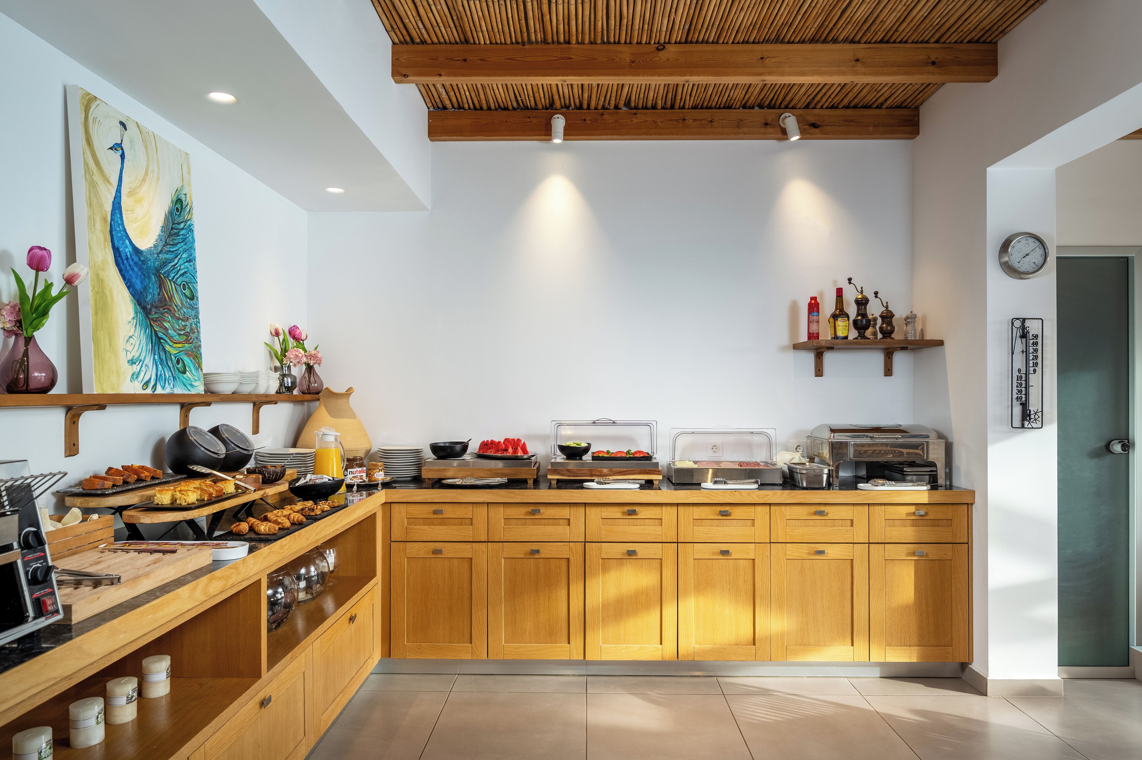 A breakfast bar with various food items, a peacock painting, and wooden cabinets.