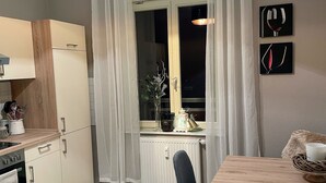 A modern kitchen with a dining area, featuring a window with curtains, a radiator, and a table with chairs. - Apartment zur Wiege Anhalts (Ballenstedt)
