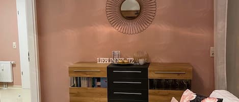 A living room with a white sofa, a wooden coffee table, a decorative mirror, and a wooden cabinet with drawers.