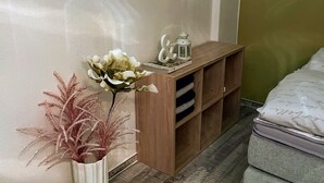 A room with a wooden side table, a white vase with flowers, a small shelf with decorative items, and a bed with a patterned bedspread. - Apartment zur Wiege Anhalts (Ballenstedt)