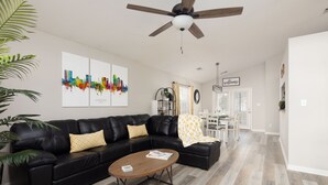 A modern living room with a black leather sofa, a wooden coffee table, and a ceiling fan. There are two framed cityscape artworks on the wall and a 'welcome' sign above the door. - Lexington Cutie! Entire house close to UK, hospitals,  and Keeneland (Lexington)