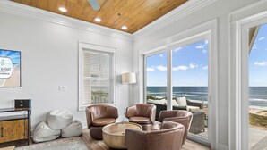 A spacious living room with leather chairs, a round coffee table, and a view of the ocean through large sliding glass doors. - Oytstercatcher: Beachfront, Private Pool, Hot Tub, Sleeps 22! (St. George Island)