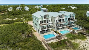 A large, multi-story beachfront property with multiple balconies, a swimming pool, and lush greenery. - Oytstercatcher: Beachfront, Private Pool, Hot Tub, Sleeps 22! (St. George Island)